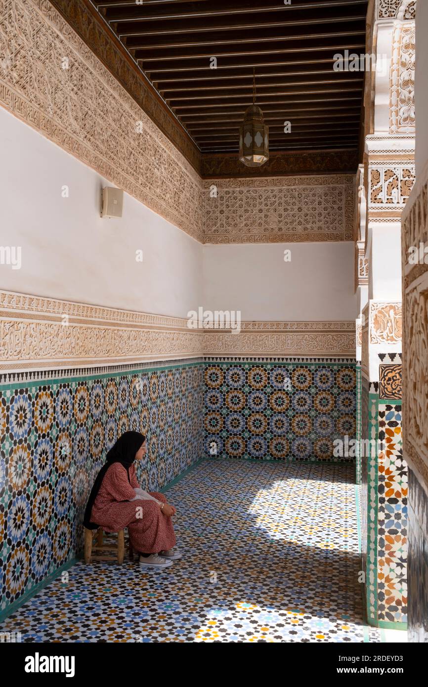 Marokko: Eine Frau, die in einer der Galerien um den zentralen Innenhof sitzt, Ben Youssef Madrasa (Medersa Ben Youssef), Medina von Marrakesch, Marrakesch. Der Sultan der Saadier-Dynastie, Abdallah al-Ghalib Billah (1517 - 1574), baute die Madrasa im Jahr 1565 (972 AH). Es war einst das größte islamische College im Maghreb (Nordwestafrika). Stockfoto