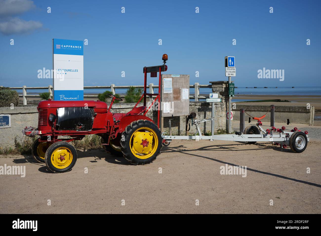 Oldtimer-Traktor in Rot mit gelben Rädern und Anhänger am Asnelles Beach. Asnelles, Frankreich Stockfoto