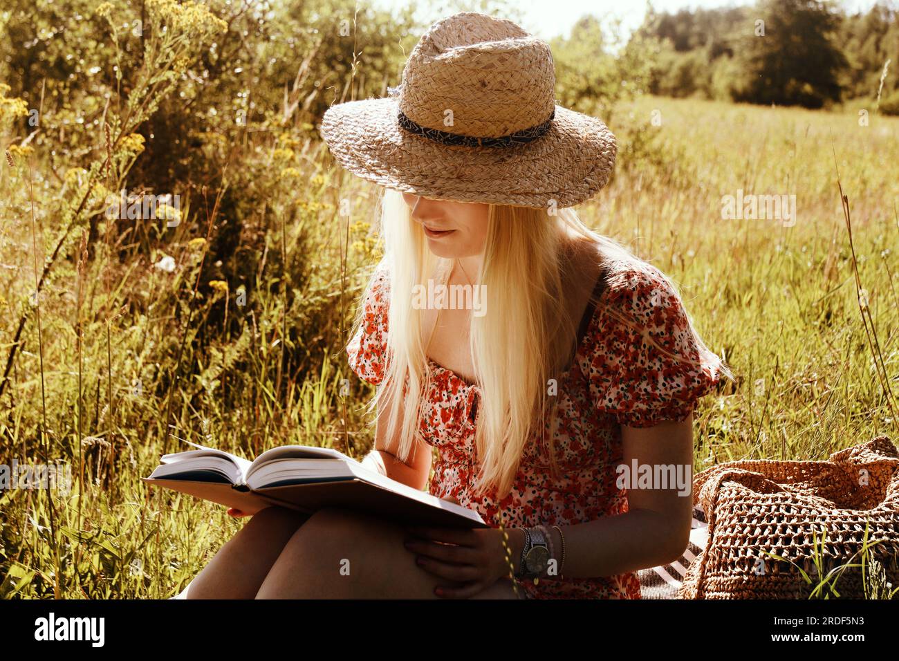 Junge blonde Frau mit Strohhut und Buch im Sommer Stockfoto