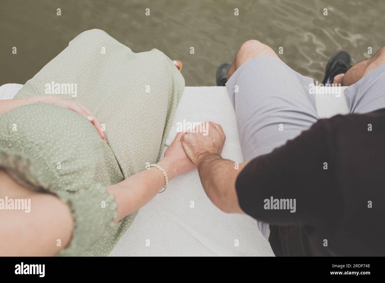 Es wird erwartet, dass ein Paar Händchen hält, während es auf dem Dock sitzt Stockfoto