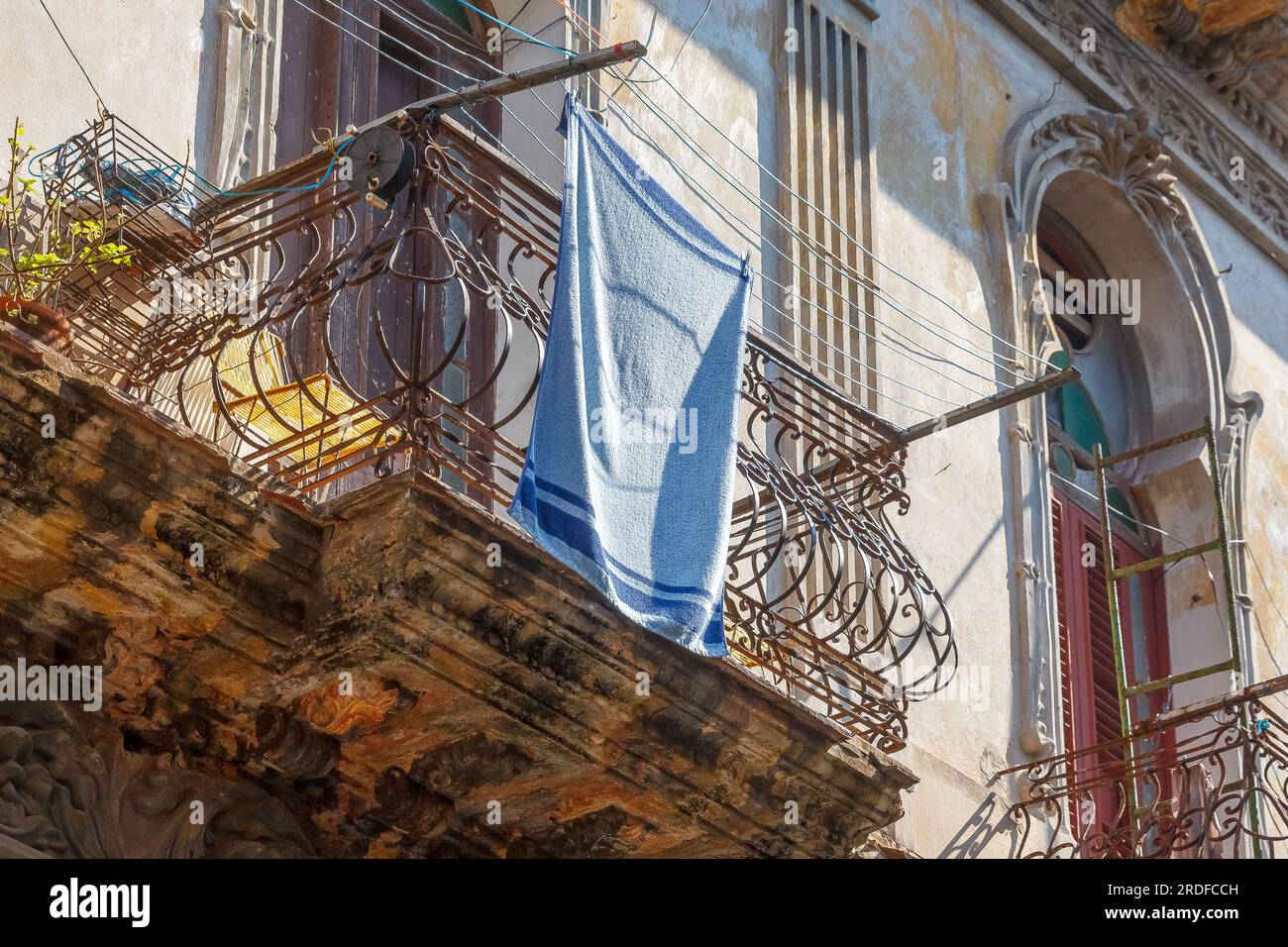 Havanna, Kuba - 27. Mai 2023: Ein blauer Turm, der im Wind trocknet. Der Textilgegenstand hängt von einem Balkon in einer verwitterten alten Gebäudefassade. Stockfoto