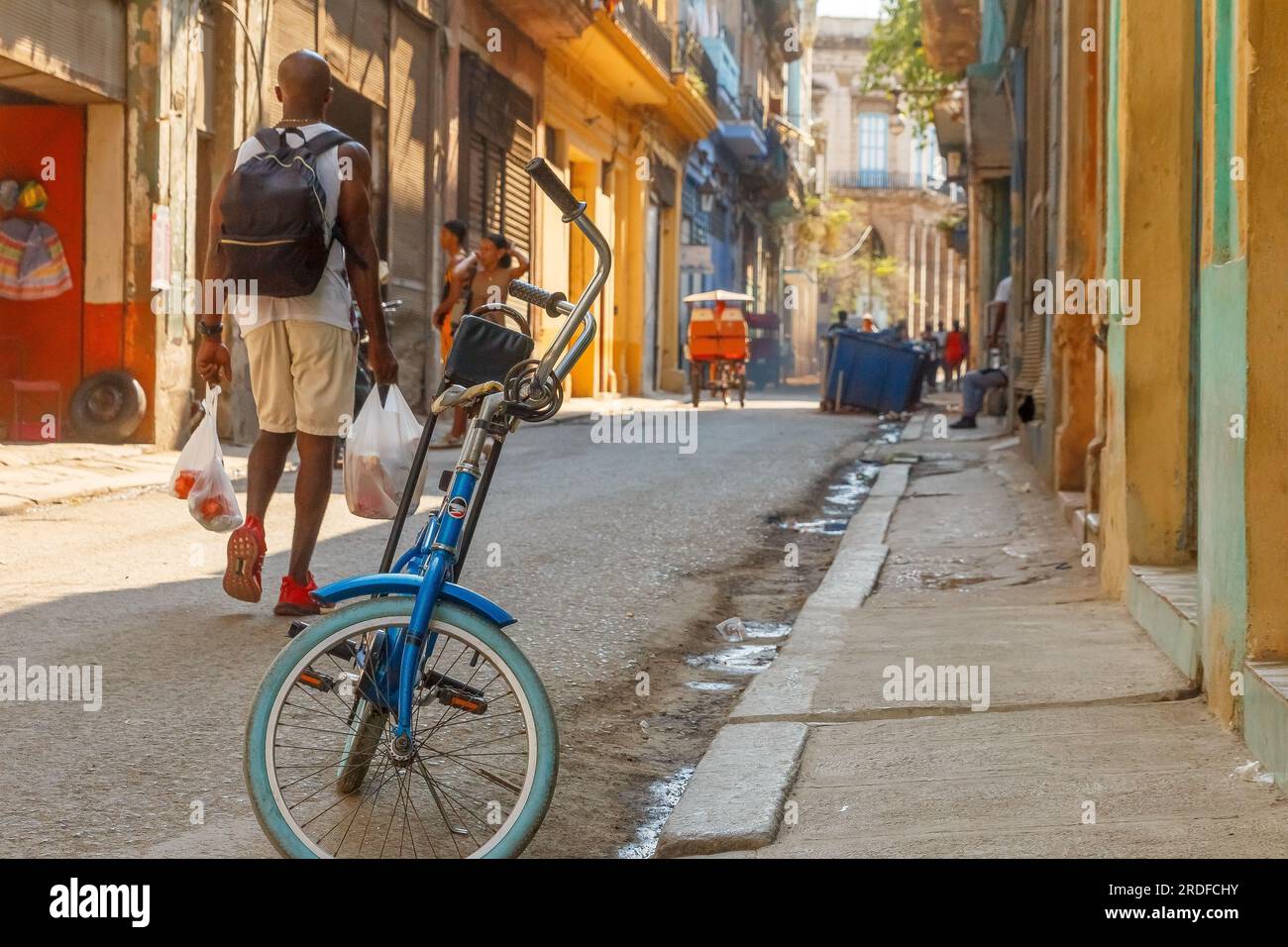 Havanna, Kuba - 27. Mai 2023: Ein afro-karibischer Mann geht mit zwei Einkaufstüten in einer Straße der Stadt. Ein Fahrrad steht am Bürgersteig. Lifest Stockfoto