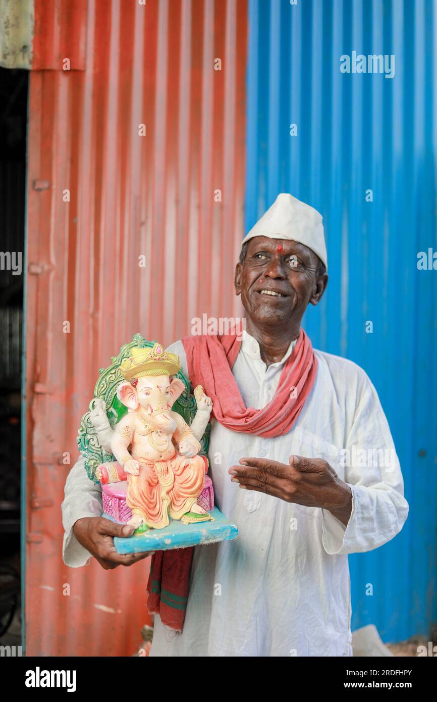 Ein alter indischer Mann, der Lord Ganesha Idol in den Händen hält, ein glücklicher, alter, armer Mann Stockfoto