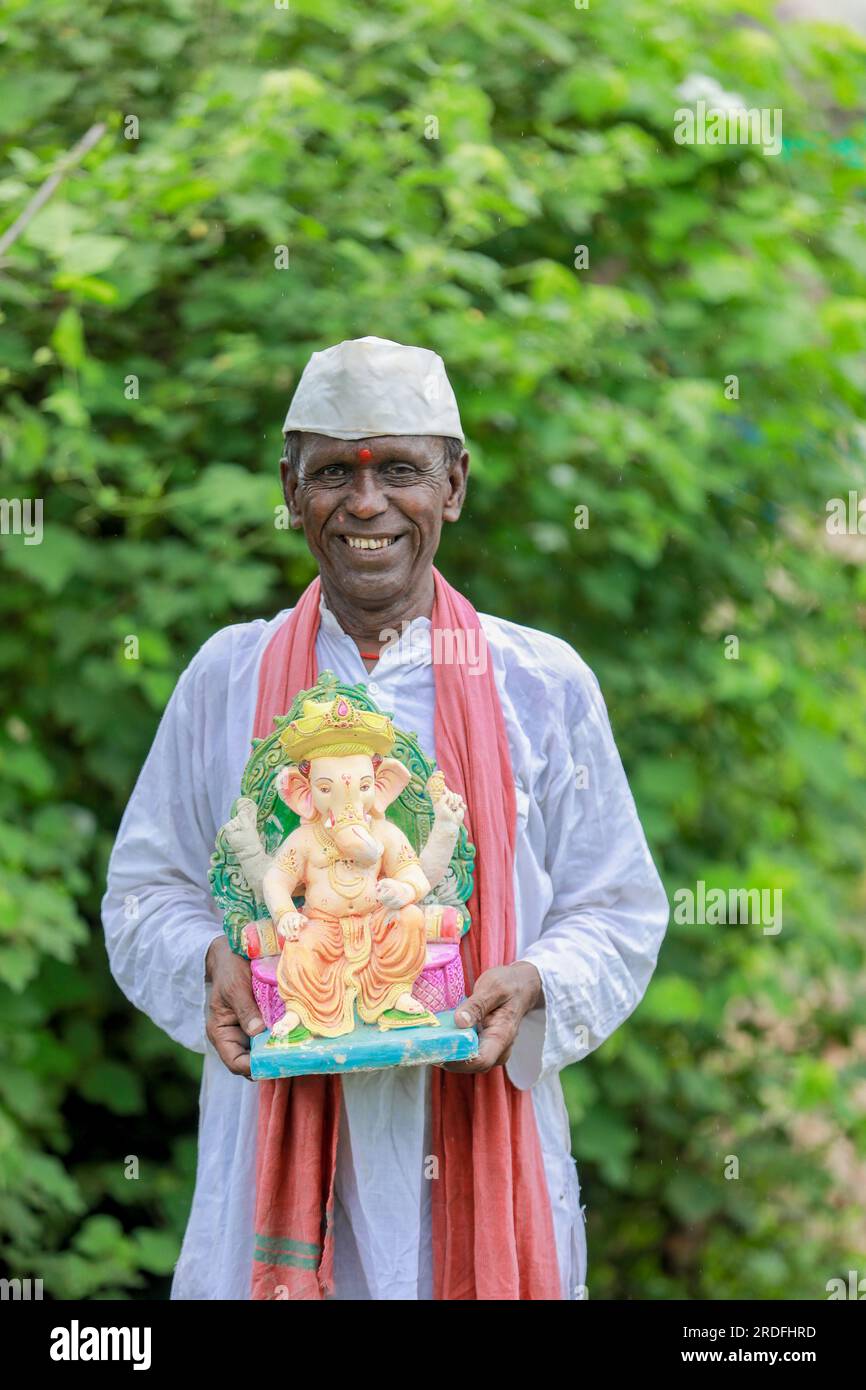 Ein alter indischer Mann, der Lord Ganesha Idol in den Händen hält, ein glücklicher, alter, armer Mann Stockfoto