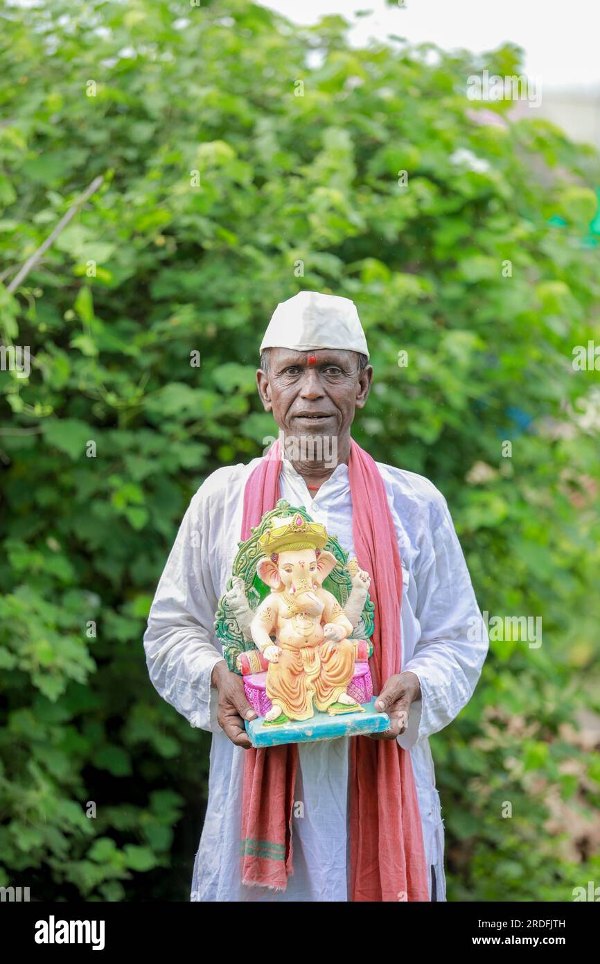 Ein alter indischer Mann, der Lord Ganesha Idol in den Händen hält, ein glücklicher, alter, armer Mann Stockfoto