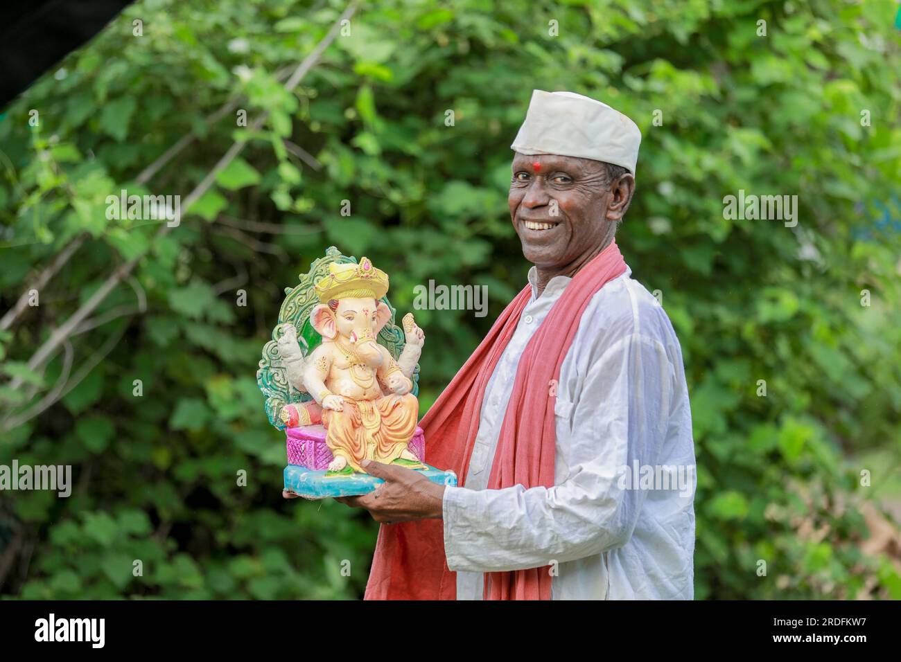 Ein alter indischer Mann, der Lord Ganesha Idol in den Händen hält, ein glücklicher, alter, armer Mann Stockfoto