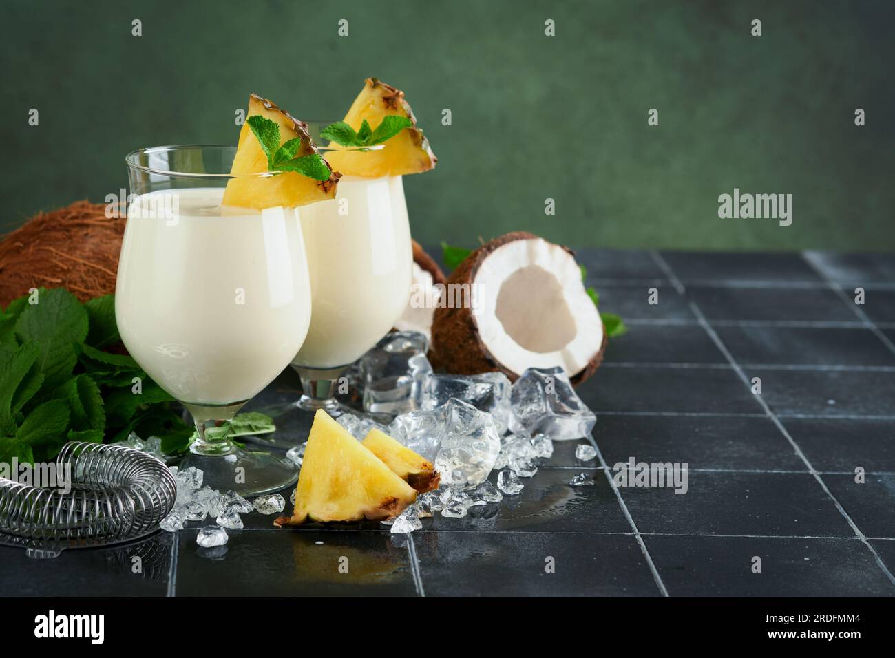 Pina Colada. Traditioneller karibischer Cocktail aus Rum, Ananassaft und Kokosnusscreme mit tropischen Früchten und Barutensilien auf frischem grünen Hintergrund. Stockfoto