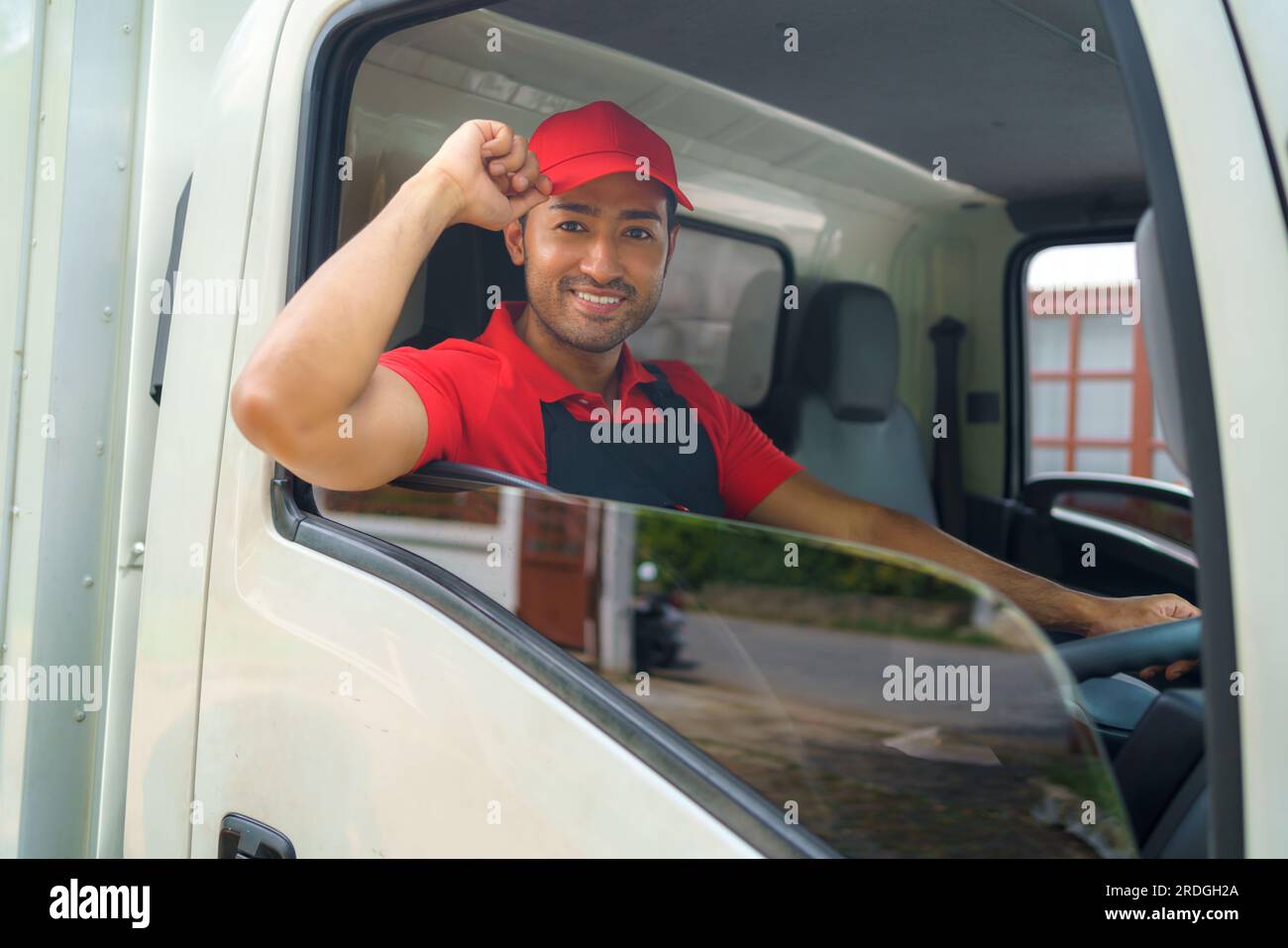 Der Transportarbeiter sitzt im Laster und lächelt vor Bereitschaft und Hingabe, während er sich auf den Weg zu einem neuen Haus macht. Ihre Begeisterung und ihr Engagement Stockfoto