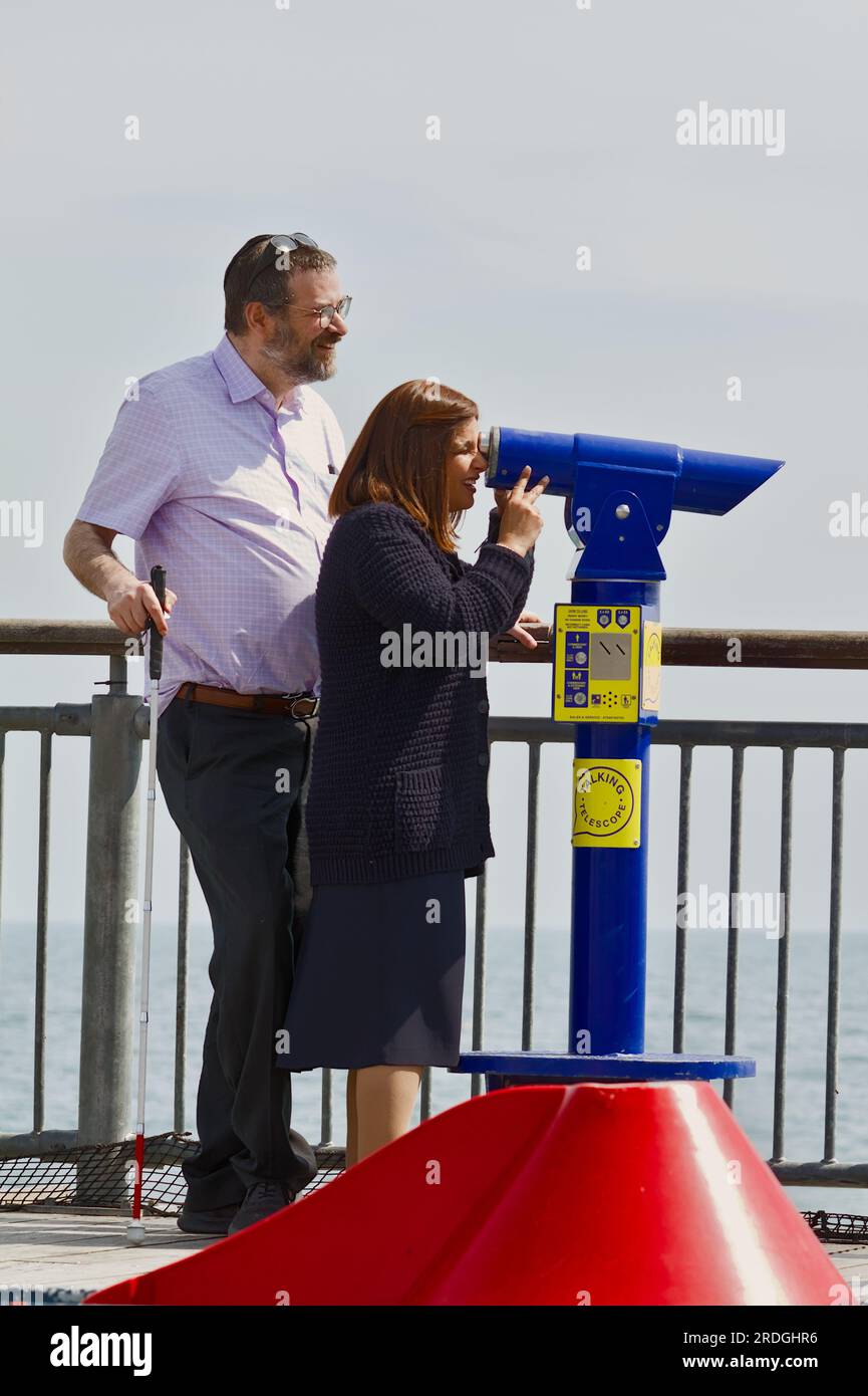 Mann und sehbehinderte Frau, die Ein münzbetriebenes sprechendes Teleskop benutzt, um die Aussicht am Ende des Bournemouth Pier, Großbritannien, zu beschreiben Stockfoto