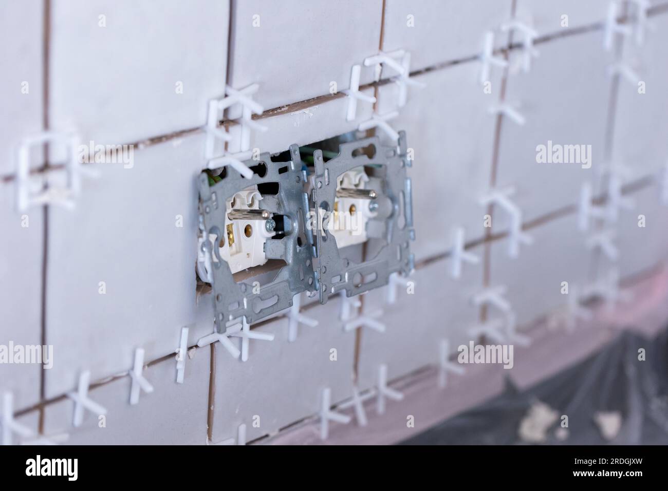 Nahaufnahme von zwei angeschlossenen Steckdosen ohne Schutzkappen in einer neu gefliesten Wand, immer noch mit dem Kunststoff-Spa mit weißem Gelenk Stockfoto