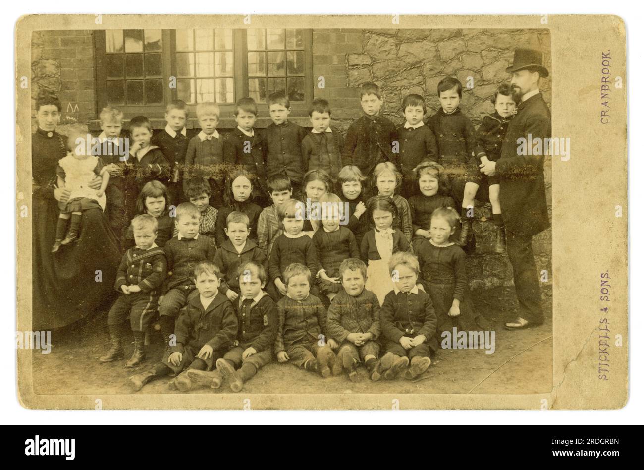 Originale charmante viktorianische Schrankkarte mit Sepia-Ton von viktorianischen Schulkindern vor einem Schulgebäude mit Schullehrern oder Lehrassistenten von Stickells & Sons, die in Cranbrook, Kent, ansässig waren. aber in Sussex und Surrey aktiv, was den Standort dieser Schule unbekannt machte, aber in Südostengland, Großbritannien, datiert 1884. Stockfoto