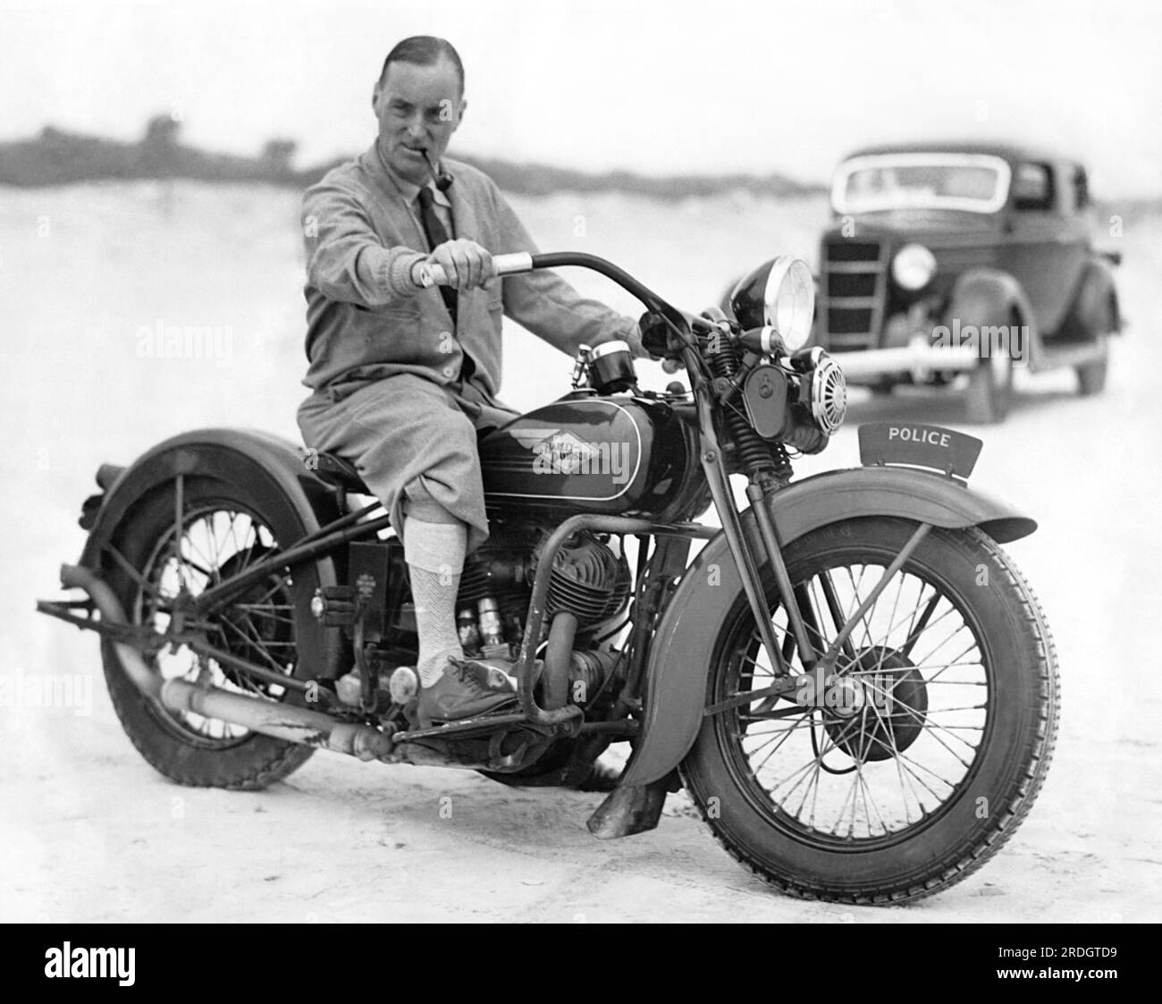 Daytona Beach, Florida: 13. Februar 1935 der britische Rennfahrer Captain Malcolm Campbell probiert die Harley Davidson eines Polizisten aus, aber er wird nicht annähernd die 300 km/h erreichen, die er in seinem Bluebird Rennwagen am Strand erreichen möchte. Stockfoto