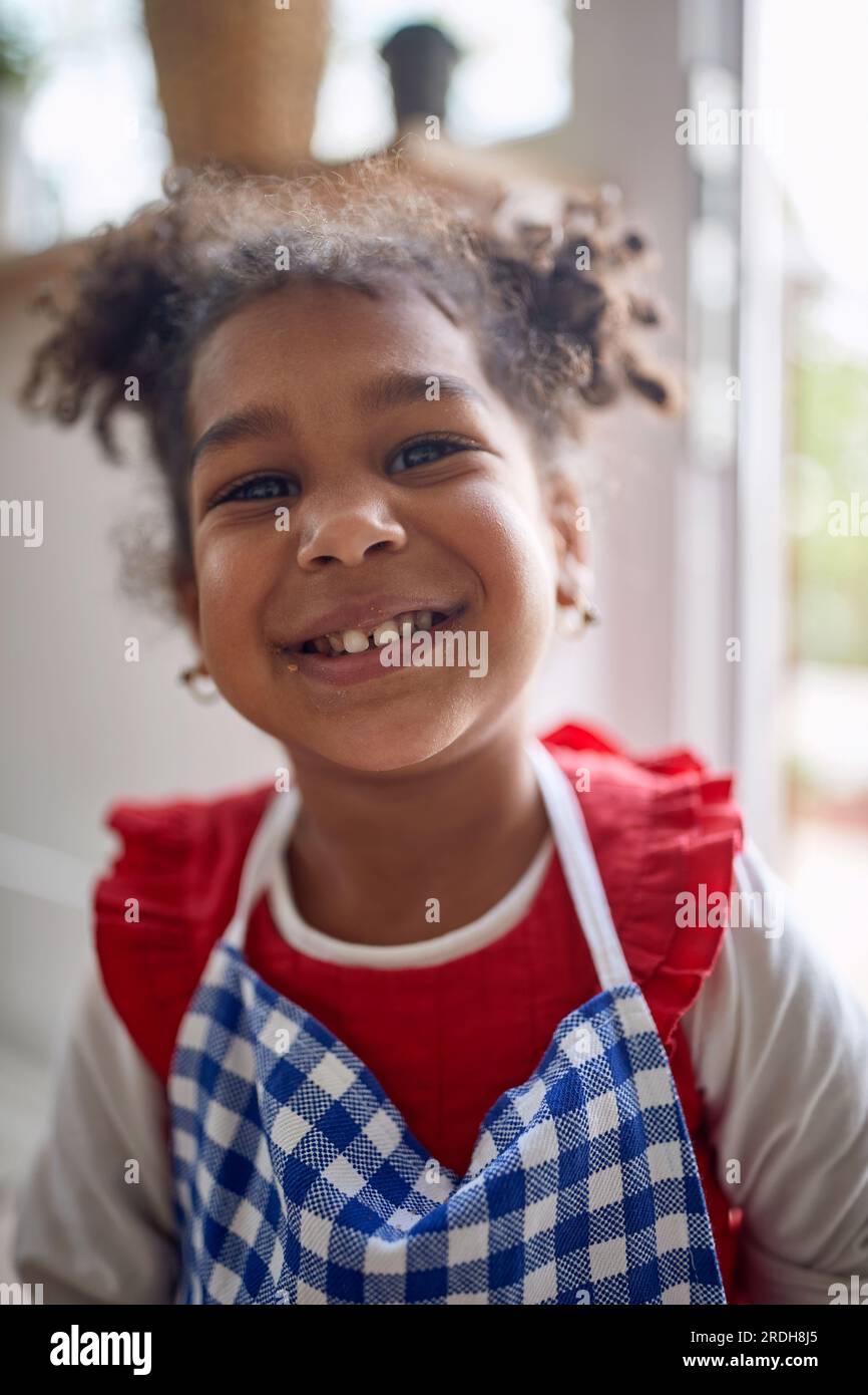 Süßes kleines Mädchen, das in einer Küche steht, eine blaue Schürze mit Schürze umhüllt und fröhlich und lächelnd ist. Das Konzept des Familienlebens. Stockfoto