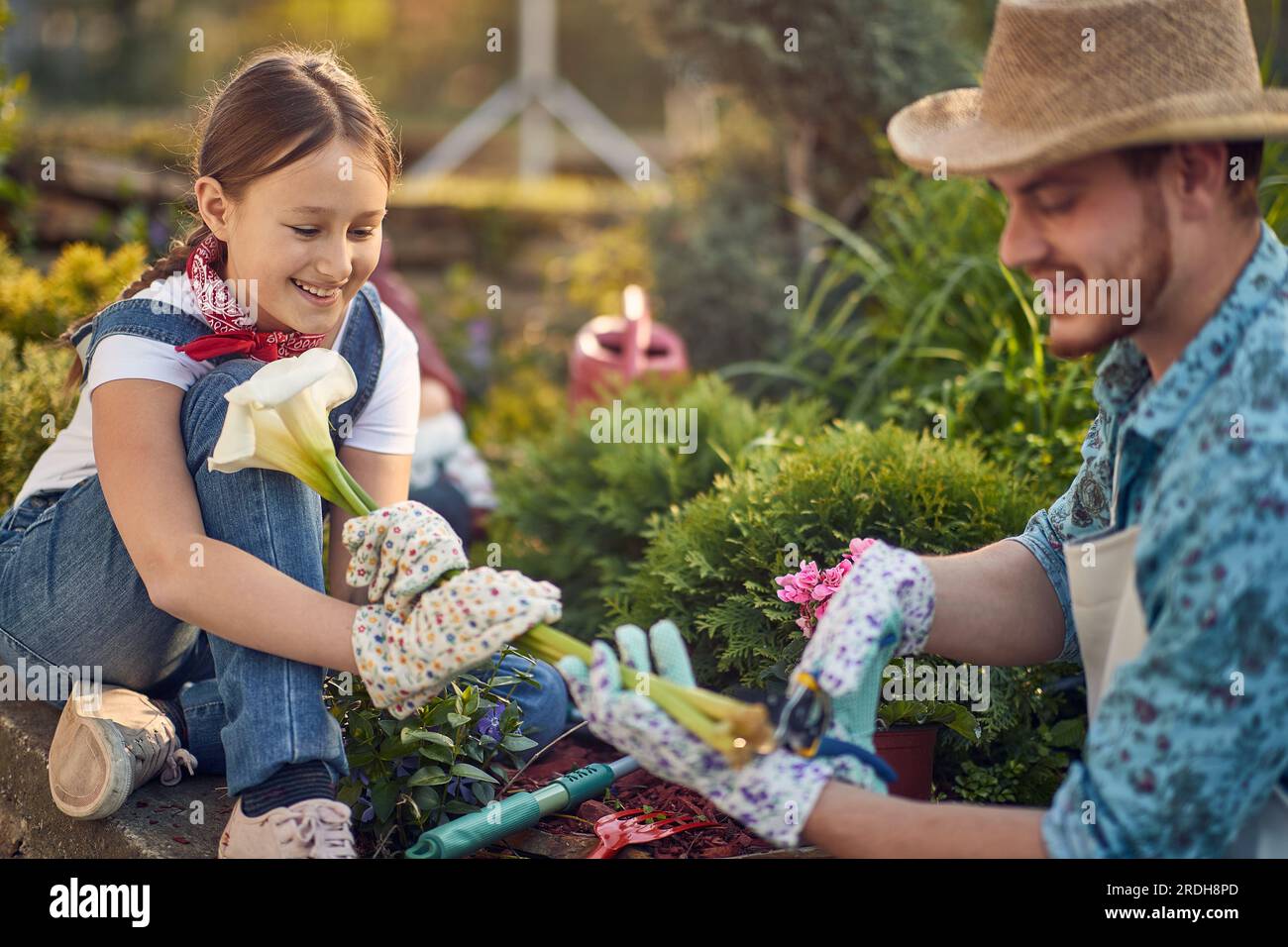 Vater und seine Tochter sind sorgfältig beschnittene Blumen. Freude und Gelassenheit dieser gemeinsamen Gartenerfahrung, die ein Gefühl der Verbindung mit der Natur fördert Stockfoto