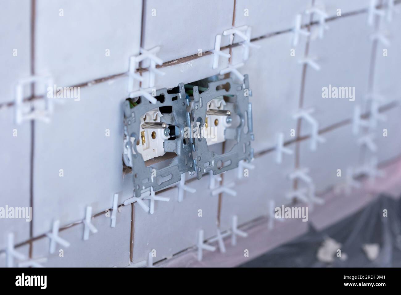 Ein Porträt von zwei angeschlossenen elektrischen Wandsteckdosen ohne Schutzkappen aus Kunststoff in einer neu gefliesten, unfertigen Wand, immer noch mit weißem Kunststoff Stockfoto