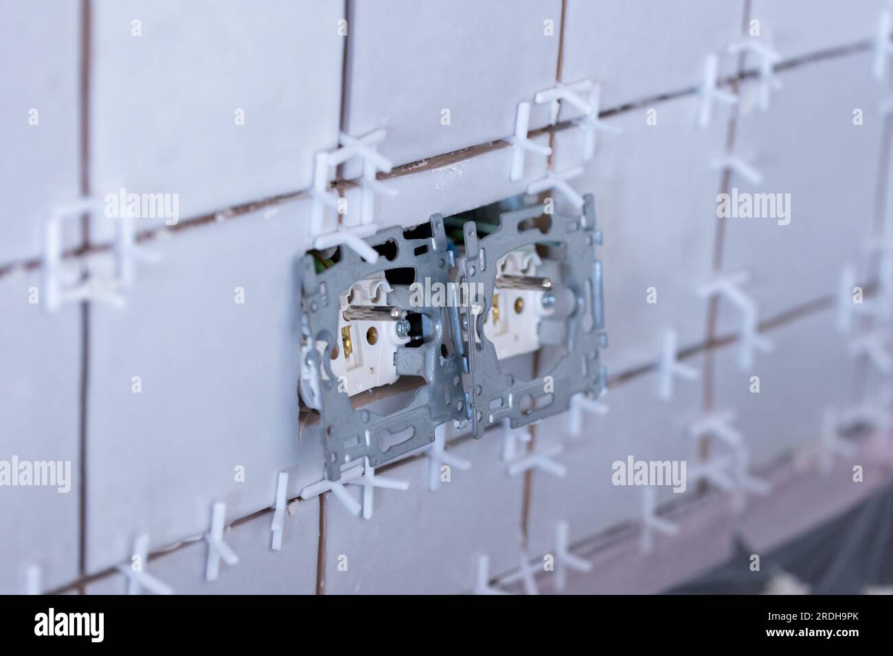 Nahaufnahme von zwei angeschlossenen Steckdosen ohne Schutzkappen in einer neu gefliesten Wand, immer noch mit dem weißen Kunststoffanschluss Spa Stockfoto