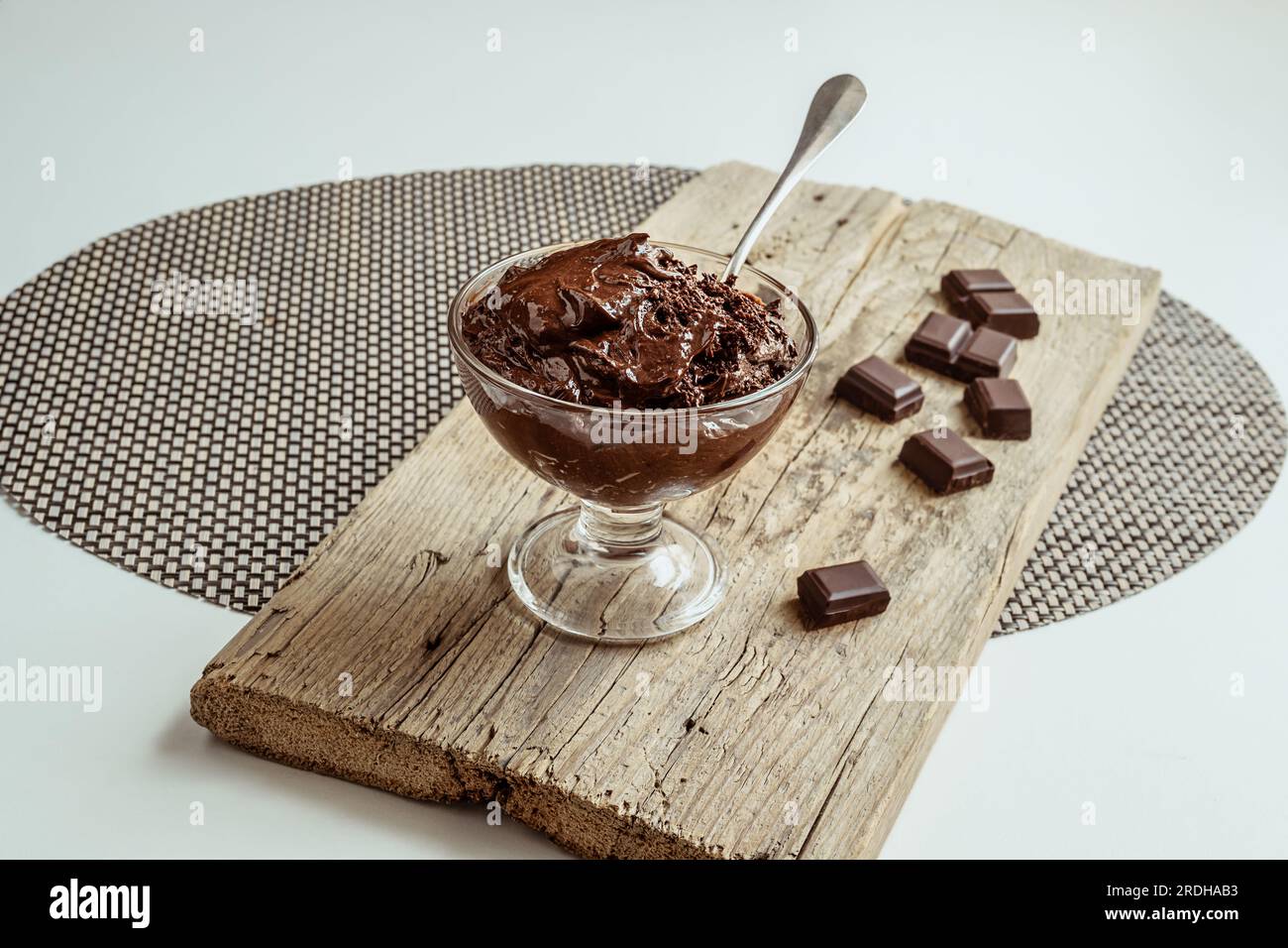 Eine transparente Schüssel mit Schokoladenmousse, traditionellem französischen Dessert und Stücken dunkler Schokolade auf einem Holzbrett Stockfoto