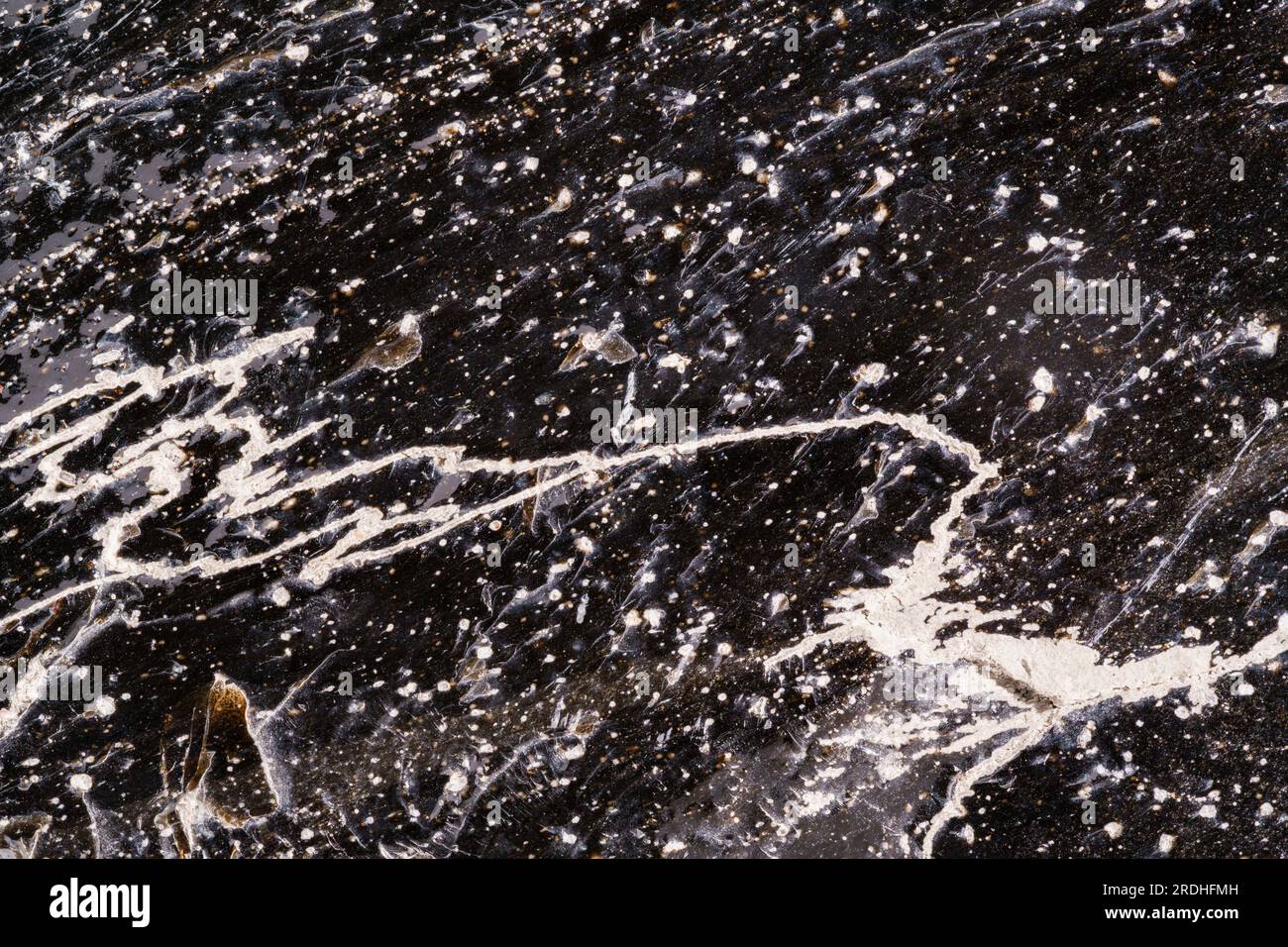 Kontrastreiches Makrofoto von Obsidian mit vielen Blasen, Farben und Verunreinigungen unter der Oberfläche. Stockfoto