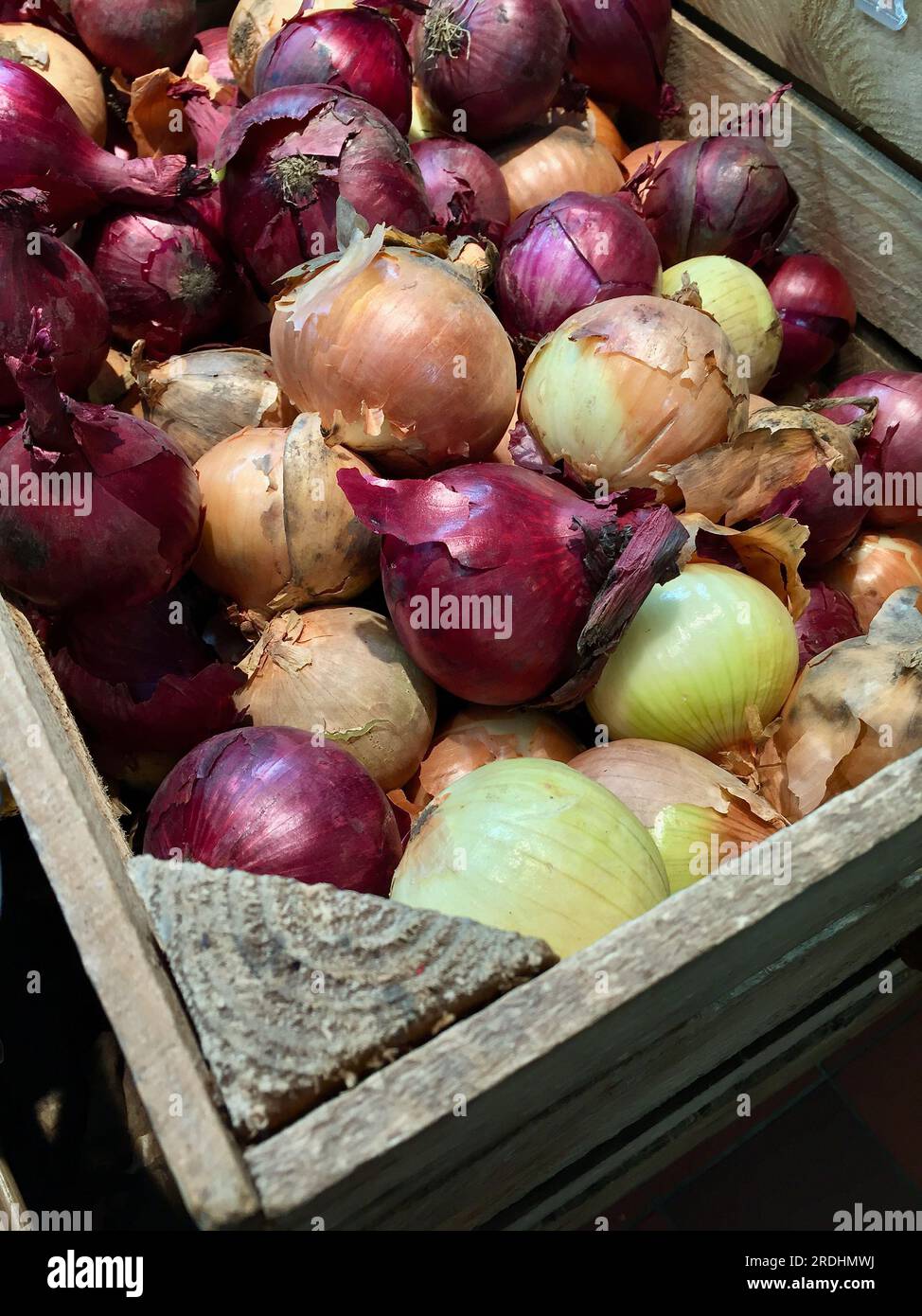 Holzkiste mit gemischten Speisezwiebeln zum Verkauf auf dem Bauernmarkt im Winter. Stockfoto