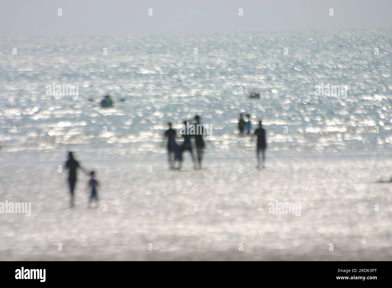 Ein verschwommenes Bild, auf dem viele Menschen im Wasser spielen und in Richtung des flachen Wassers gehen. Himmel und Meer haben fast die gleiche Farbe und das Stockfoto