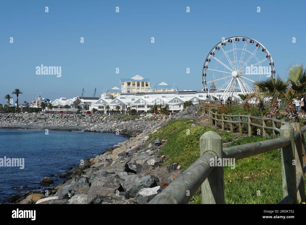 Lebhaftes Hafenviertel in Kapstadt hinter einer romantischen blauen Bucht mit Steinstrand. Stockfoto