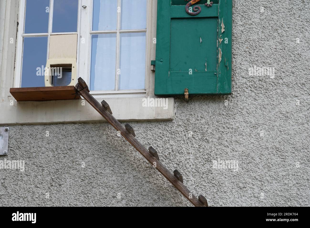 Eine Hauswand mit einem Fenster mit grünen Fensterläden und einer Holzleiter. Stockfoto