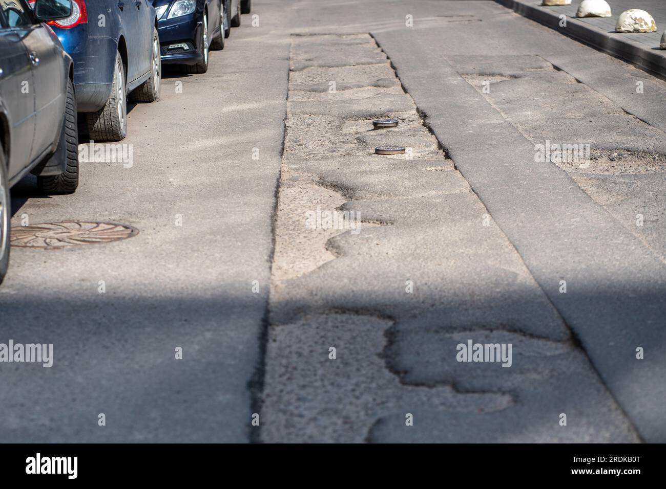 Gebrochene Asphaltstraße in der Stadt und vorzeitige Reparaturen auf dem Parkplatz, Schlaglöcher Asphaltstraßenreparaturen. Stockfoto