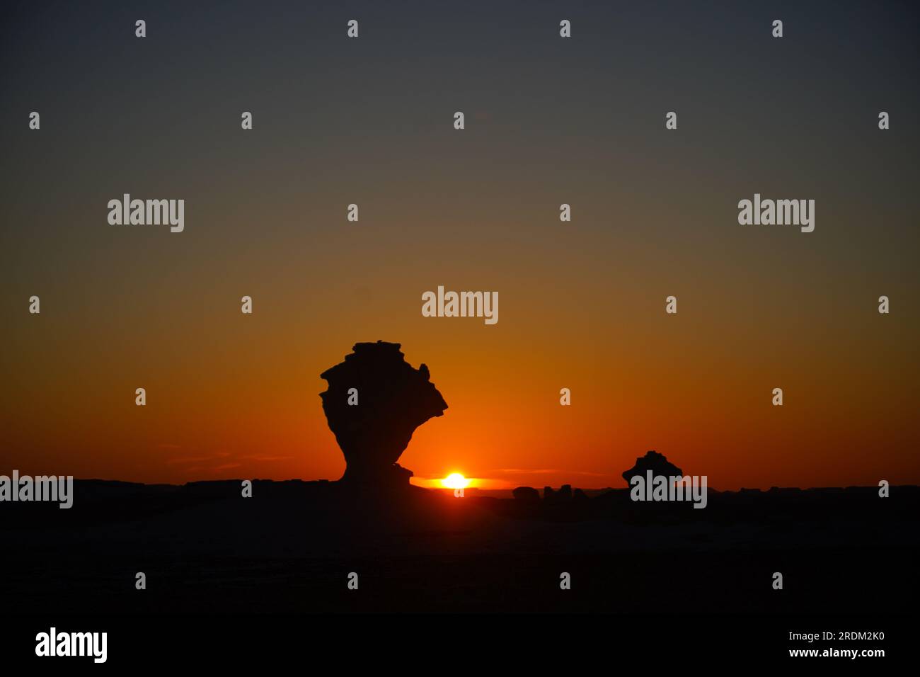 Sonnenuntergang in der Weißen Wüste, Ägypten. Von der Erosion von Vulkanen und einem Quarzberg bis hin zu verwitterten Felsen und weißen Kreidefelsen ist die Schwarze und Weiße Wüste Teil der Frarafra-Depression in der Sahara und liegt im westlichen Teil Ägyptens. Die weite Wüste führt zu den Hauptstraßen in der Nähe der libysch-ägyptischen Grenze, wo sie jetzt mit militärischer Präsenz schwer bewaffnet ist. Die bizarre natürliche Landschaft, die vor Millionen Jahren von einem Meeresboden aufstieg, ist jetzt mit Karstkalkstformationen übersät, die der Oberfläche anderer Planeten im Universum ähneln. Stockfoto