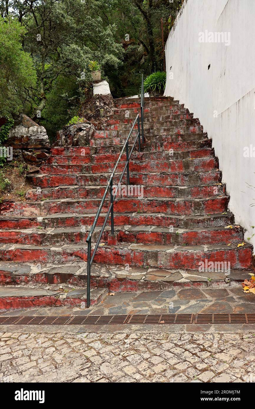Treppe mit Steintreppe, rot lackiertem Zement und einem zentralen Eisengriff. Zugang zum Heiligtum Nossa Senhora da Piedade, Lousã, Portugal. Stockfoto