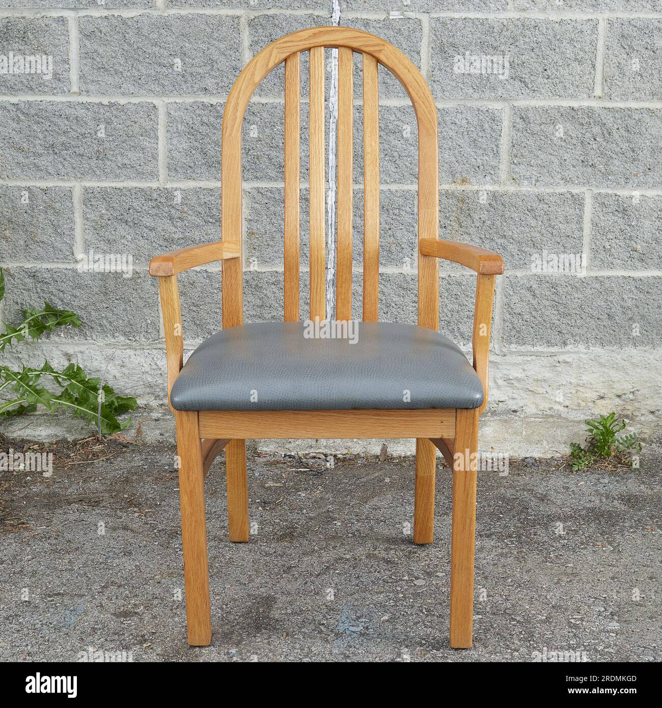 Eichensessel, einzelner heller Holzstuhl mit grauen Lederpolstern. Vorderansicht. Fotografiert vor grauem Ziegelhintergrund. Stockfoto