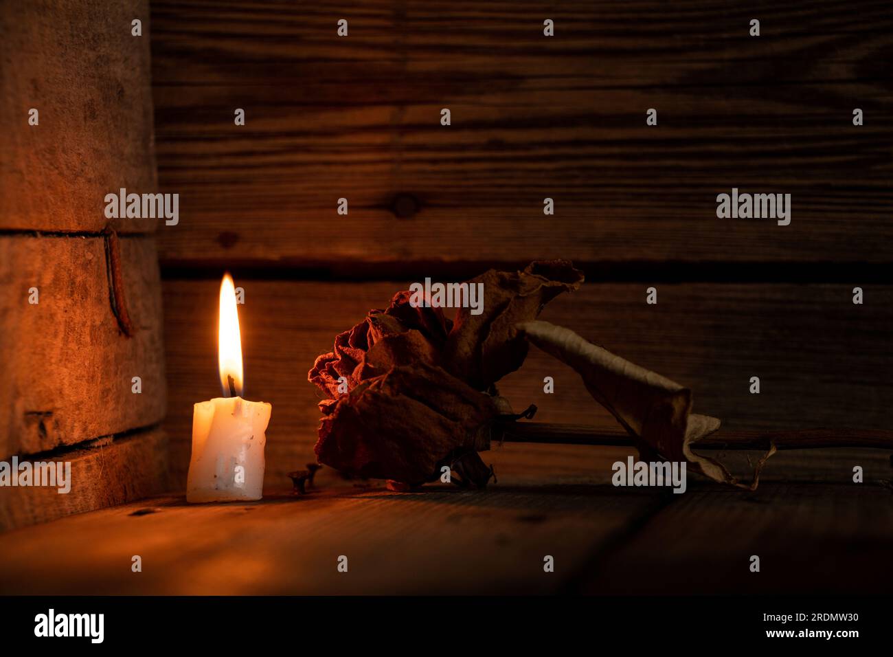 Kerzenflamme und trockene Rose in einer Ecke eines dunklen Raumes auf einem Holzboden, trauernd Stockfoto