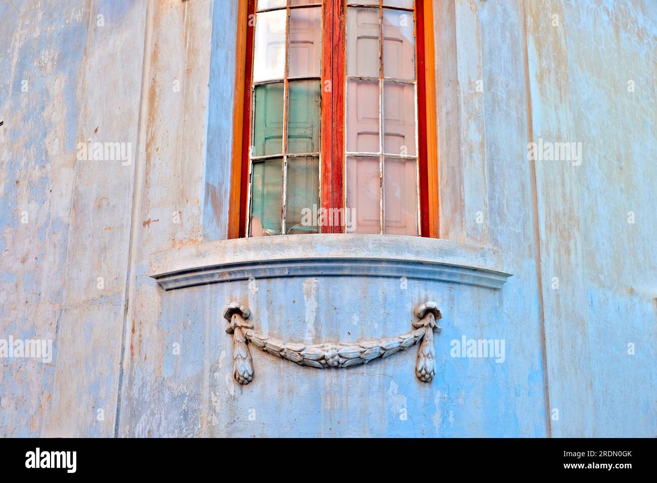 Abstraktes Architekturdetail: Ein wunderschönes Eckfenster mit warmem goldenen Holzrahmen und Zierpflaster darunter, umgeben von Pastellblau Stockfoto