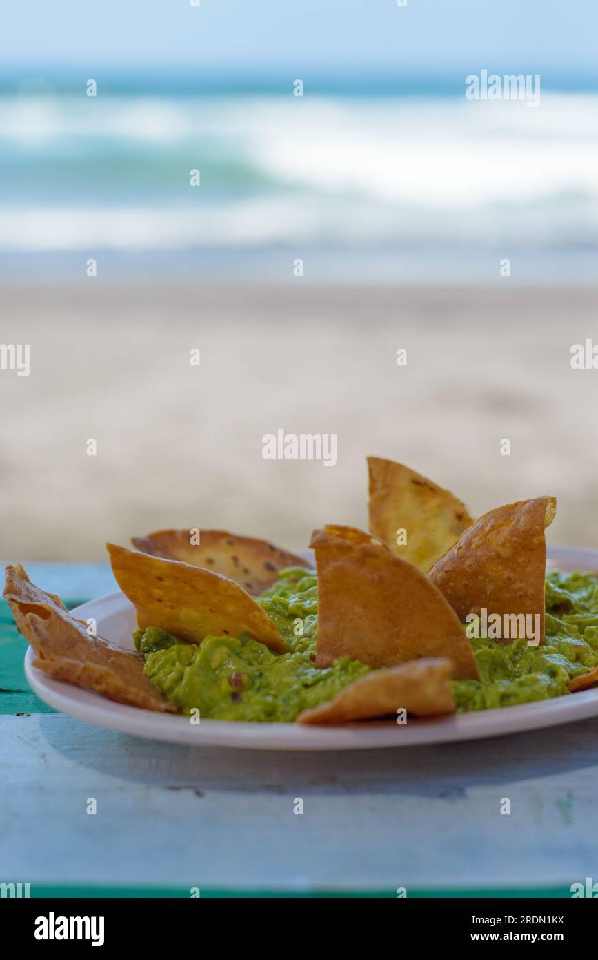 Guacamole mit Tortilla-Chips, Strandhintergrund an einem sonnigen Tag. Stockfoto