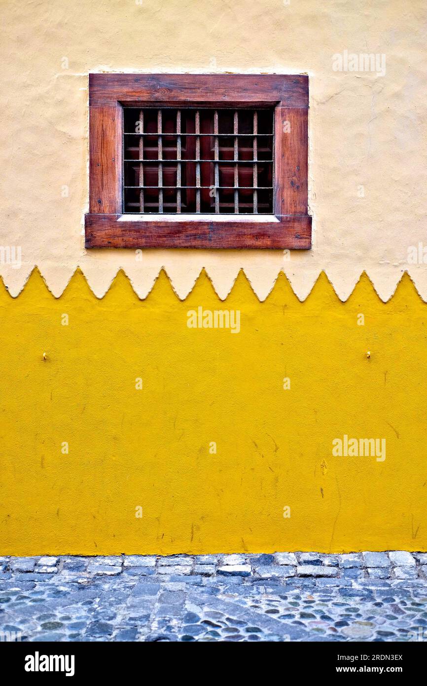 Wunderschönes kleines Fenster in einem dicken Holzrahmen, eine Wand eines Gebäudes im afrikanischen Architekturstil. Stockfoto