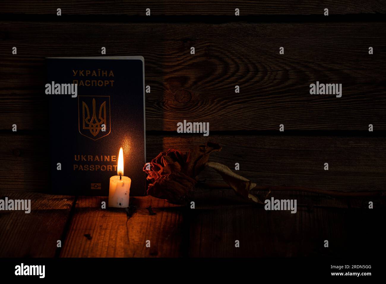 Ein ausländischer biometrischer Pass der Ukraine steht auf einem Holzboden neben Kerzenflamme und trockener Rose, trauert um die Toten Stockfoto