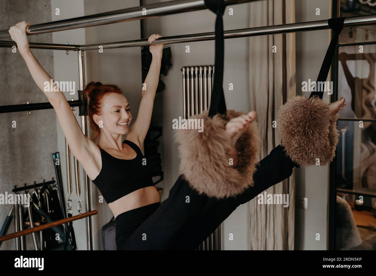 Glückliche Frau streckt sich auf dem Pilates-Reformer, genießt Bewegung, schwingt mit den Armen. Aktive Lebensweise. Stockfoto