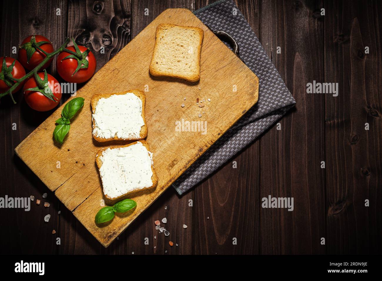 Frühstücksfoto mit Frischkäse und Brotscheiben. Tomate auf Holzhintergrund. Stockfoto