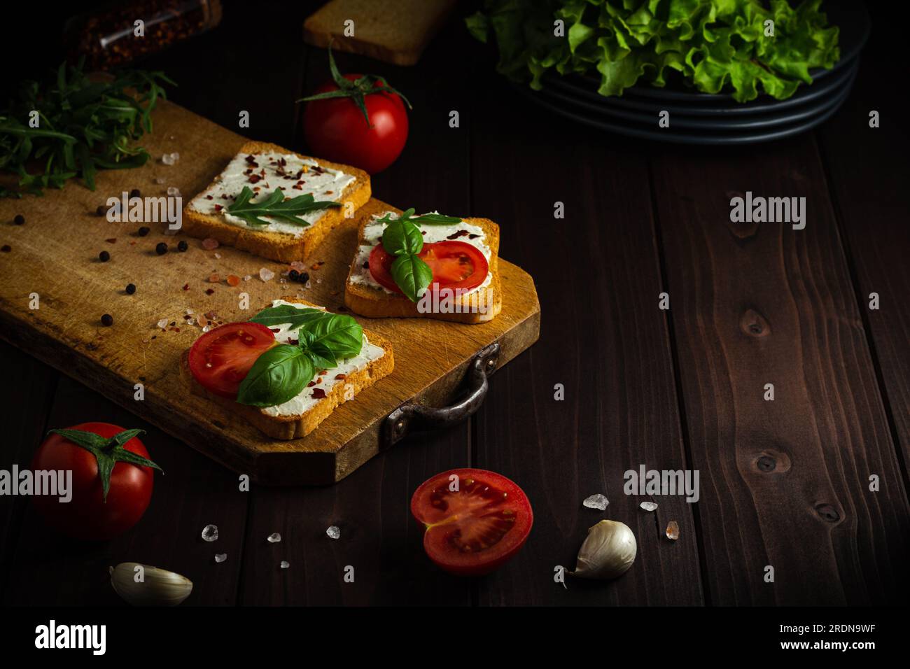 Hausgemachtes Sandwich mit Frischkäse, Salat und Tomaten auf knusprigem Roggenbrot auf dunklem Holzhintergrund mit Kopierraum Stockfoto