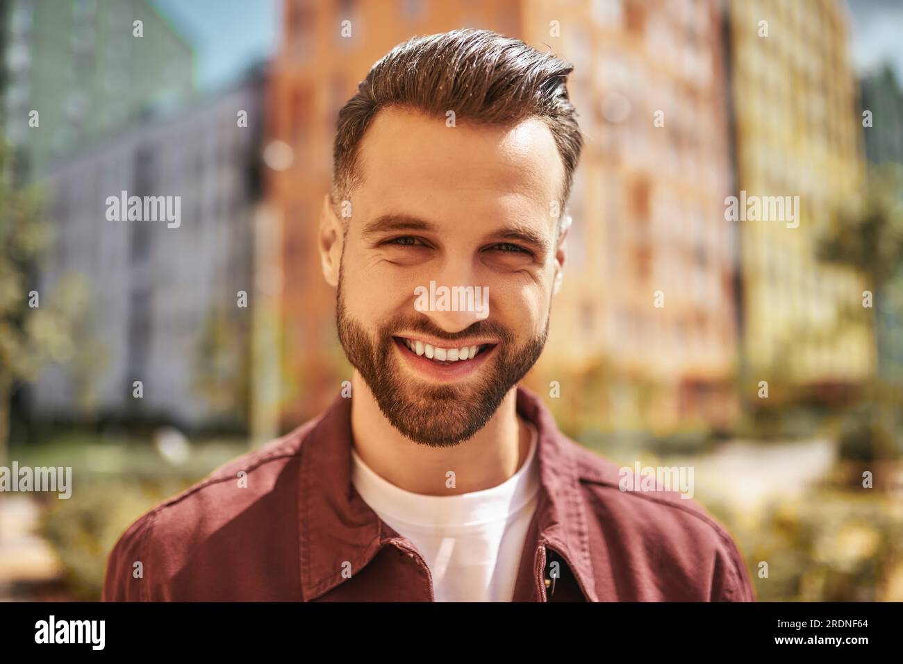 Hallo Porträt eines glücklichen, attraktiven Mannes mit lächelnden Stoppeln und Blick in die Kamera, während er auf der Straße steht Stockfoto