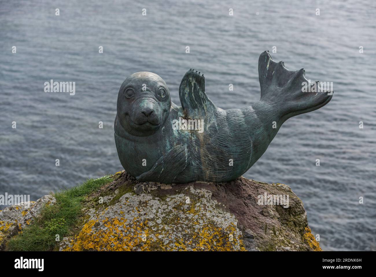 Bronzestatue eines lächelnden Seehundflossen in humorvoller Pose auf einem mit Flechten bedeckten Felsen im Hafen von North Berwick mit unscharfem Meer im Hintergrund Stockfoto