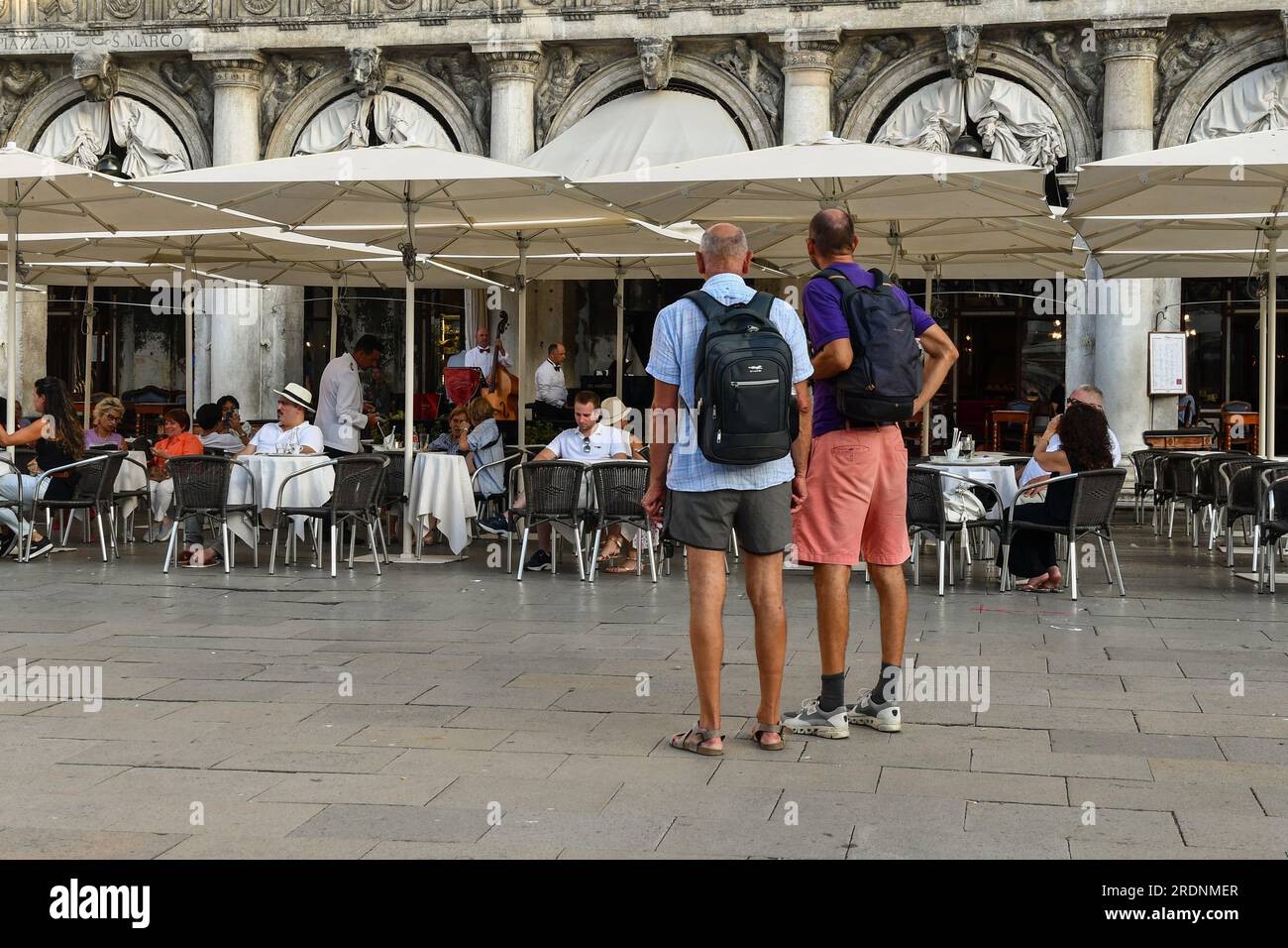 Zwei Rucksacktouristen von hinten vor dem historischen und luxuriösen Café Caffé Florian am Markusplatz im Sommer, Venedig, Veneto, Italien Stockfoto