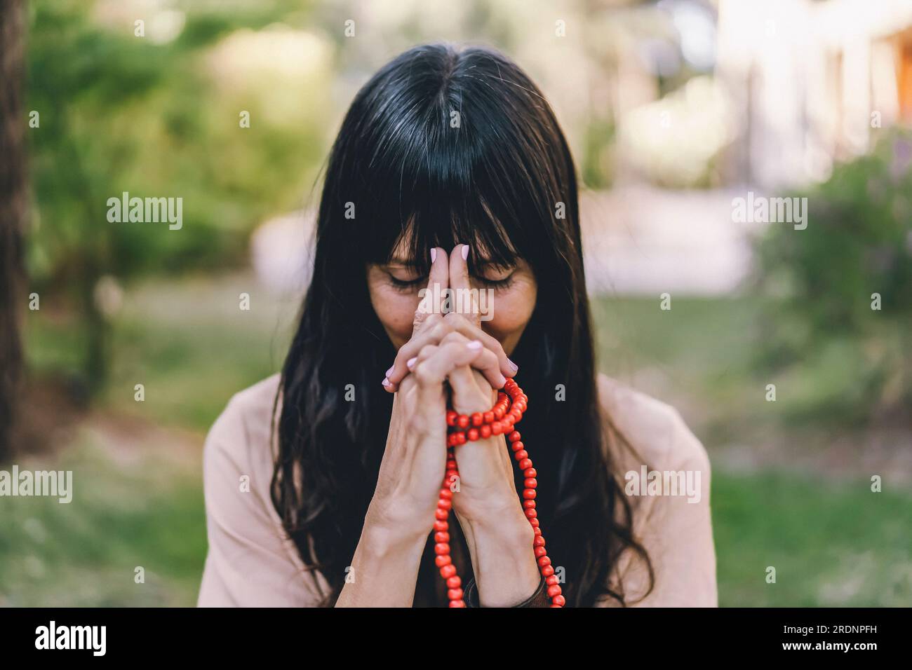 Eine Frau, die Meditation praktiziert, sitzt im Yoga asana Kali Mudra und hält eine japa mala draußen. Stockfoto