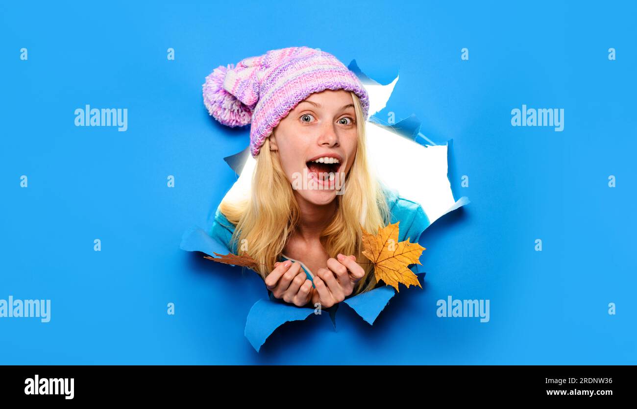 Überraschte Frau in Strickmütze mit Herbstblättern, die durch das Papierloch blickten. Herbstverkäufe. Rabatt. Saisonverkäufe. Erstauntes Mädchen im trendigen Herbst Stockfoto