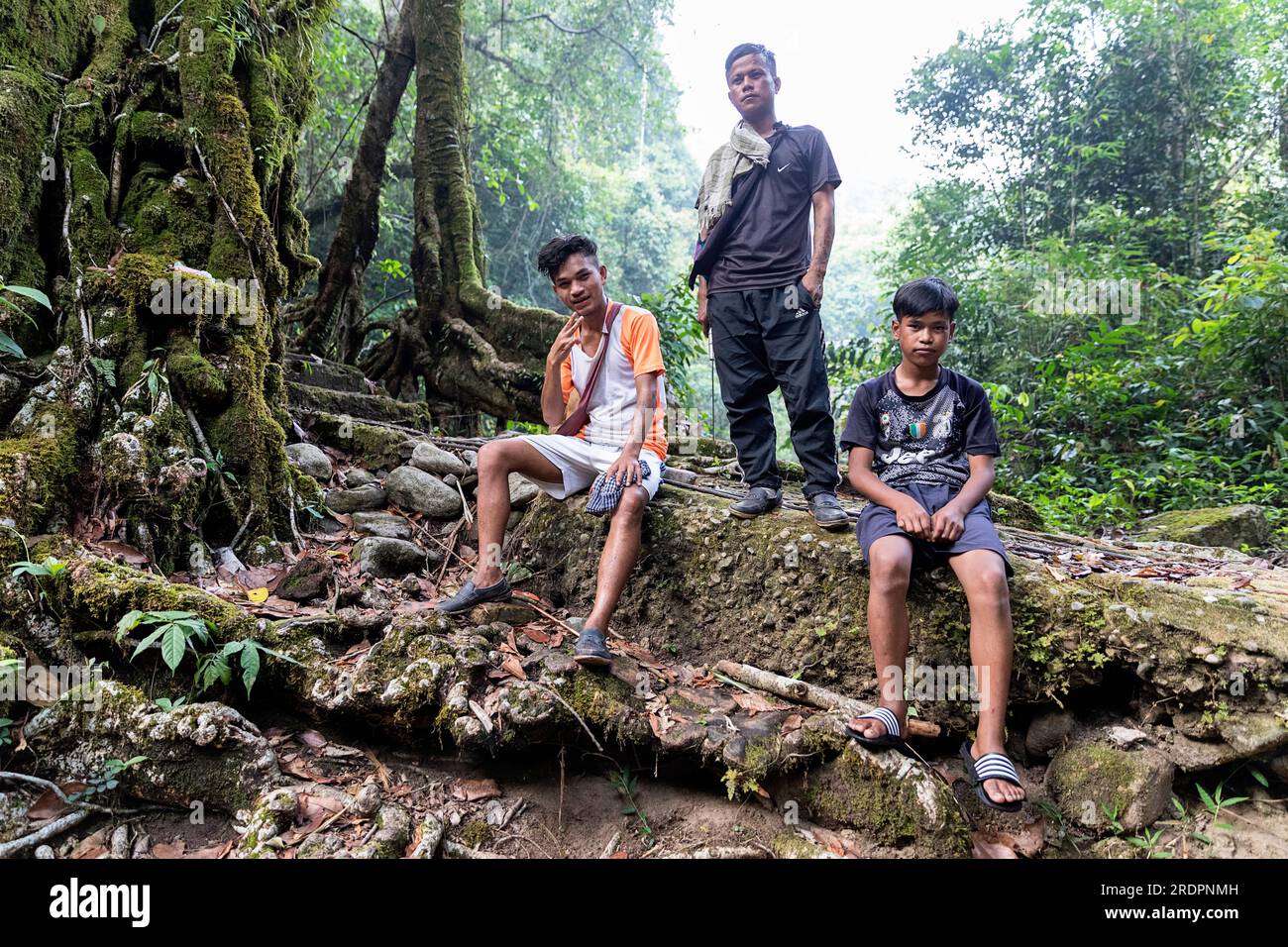 Einheimische Männer sitzen auf einem großen Felsen an der doppelten lebenden Wurzelbrücke in der Nähe des Dorfes Padu in Meghalaya, Indien Stockfoto