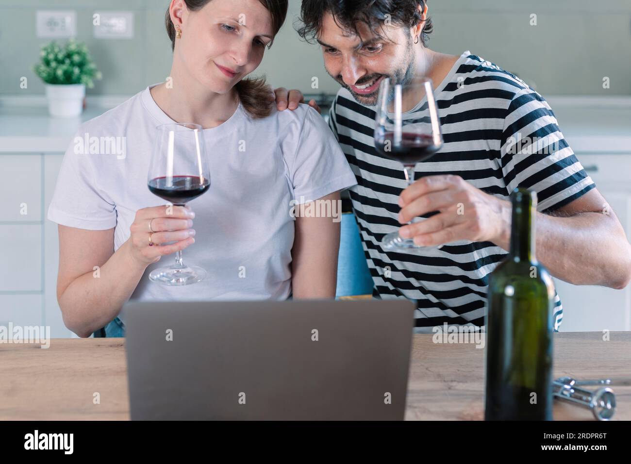 Virtuelles Partykonzept. Lächelndes Paar sitzt am Tisch und führt Online-Videogespräche mit Freunden oder Familie, die ihren Laptop benutzen, Wein und Toasti trinken Stockfoto