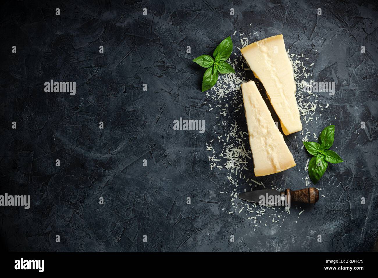 Hartkäse mit Basilikum auf dunklem Hintergrund, Hartkäse, für Textansicht von oben. Stockfoto