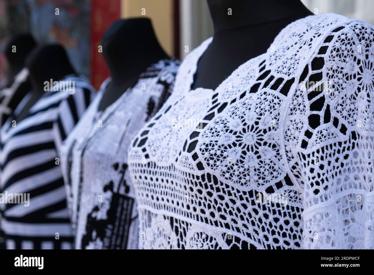 Weiße Spitzenoberteile auf schwarzen Modepuppen vor einem Schaufenster Stockfoto