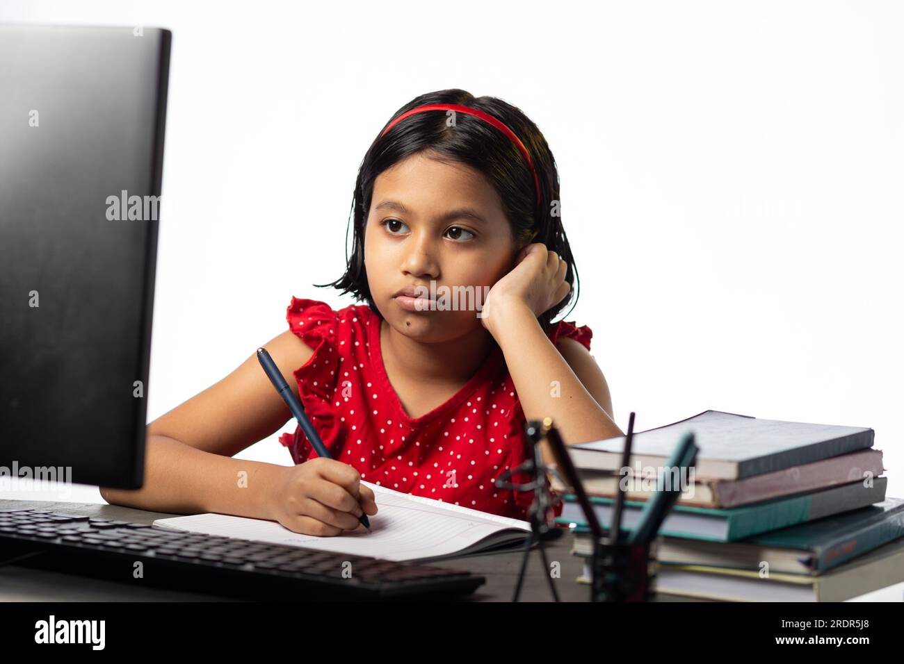 Ein hübsches indisches Mädchen, das mit einem Desktop-Computer am Arbeitstisch auf weißem Hintergrund lernt Stockfoto