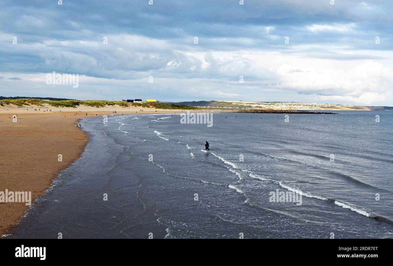 Sandy Bay und Flut kommen in Porthcawl an einem sonnigen Juli Abend, wobei der Himmel grau und bewölkt ist und viele Leute am Strand sind Stockfoto