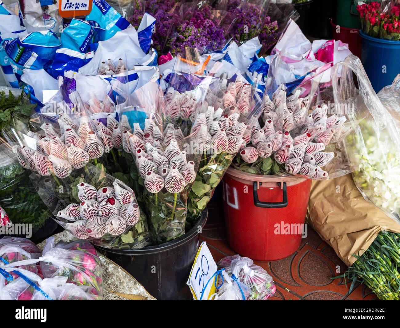 Auf dem belebten Blumenmarkt von Bangkok, Thailand, heben sich die leuchtenden roten Rosen hervor, wenn sie verpackt und zum Verkauf vorbereitet werden, was potenzielle Käufer verlockt Stockfoto